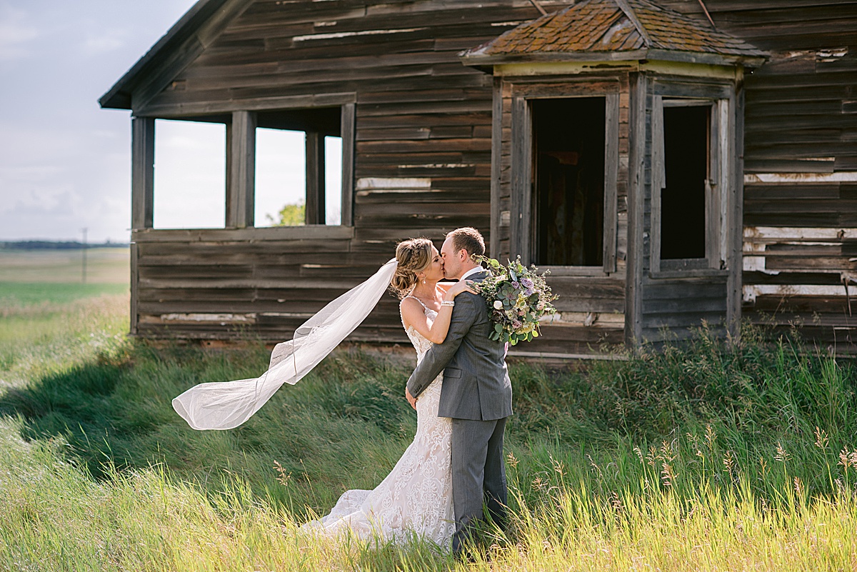 Bride and Groom portraits in front of a rustic old building with bride's veil billowing in the wind